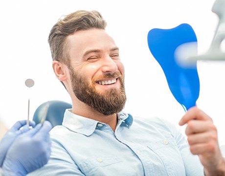 man in dental chair admiring his smile in a mirror